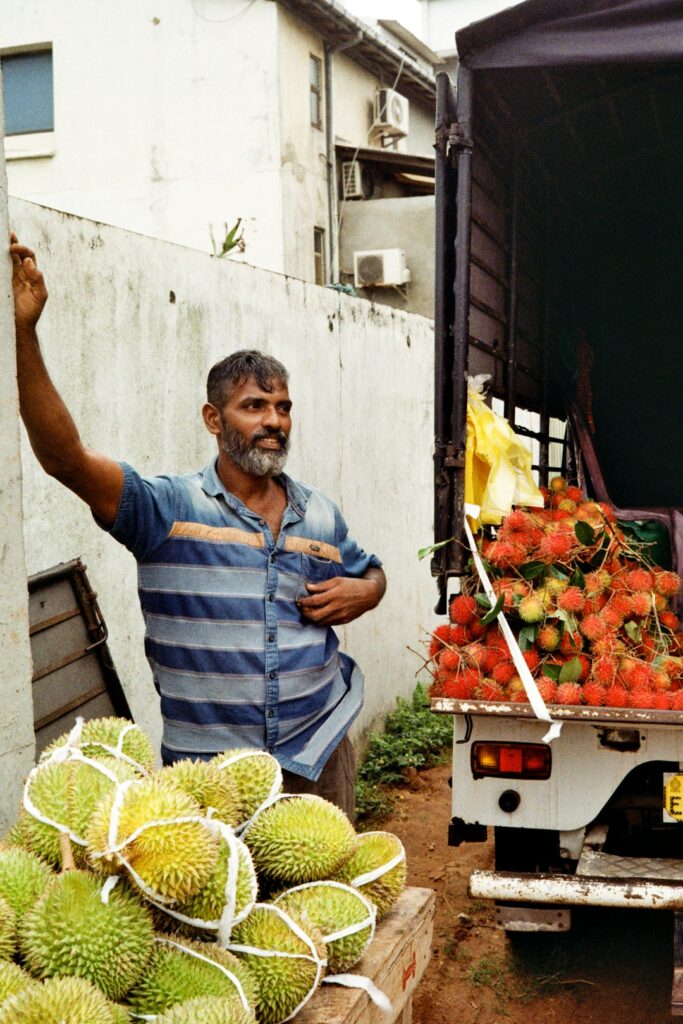 Man standing by truck with durian and rambutan fruits