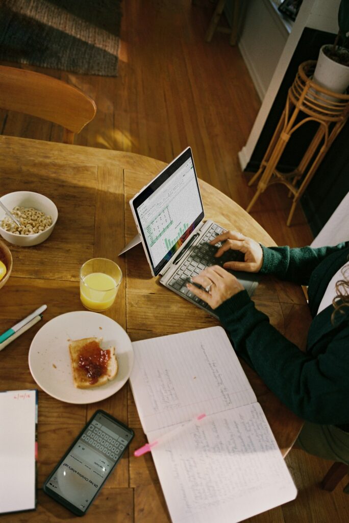 Person working on laptop at wooden table with breakfast.