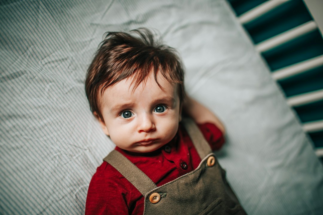 boy in red and brown jacket lying on white textile